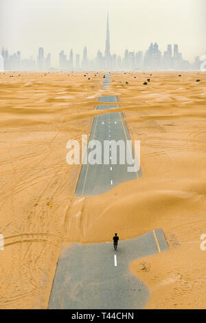 Stunning aerial view of an unidentified person walking on a deserted road covered by sand dunes in Dubai desert. Dubai skyline surrounded by fog