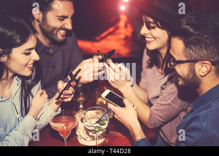 Happy friends using mobile phone and having fun with cocktails in a jazz bar - Young people addicted to new smartphone technology Stock Photo