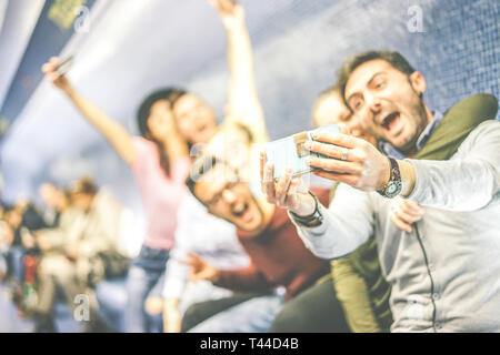 Happy friends taking a photo selfie using mobile smart phone camera sitting in a underground - Group of young people having fun taking self photos Stock Photo