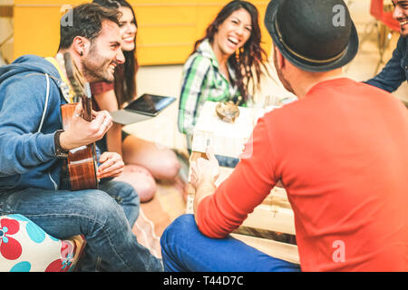 Group of friends having fun in living room in their home - Happy young people playing music with guitar and tablet singing and laughing together Stock Photo