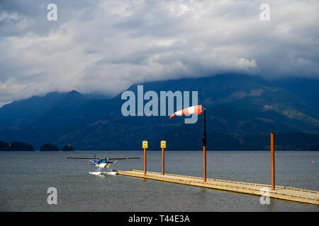 Hydroplane tied to the water aerodrome on Harrison Lake and the wind blowing into a windsock over blue and cloudy sky in Harrison Hot Springs, British Stock Photo