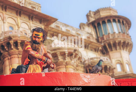 Sadhu baba sitting at Varanasi Ganges ghat with ancient architecture building as the backdrop. Stock Photo