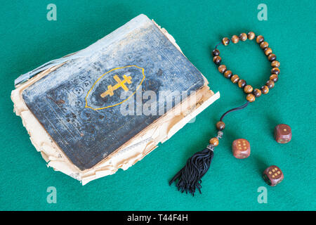 old psalm book, worry beads and three wooden dices on green baize table Stock Photo