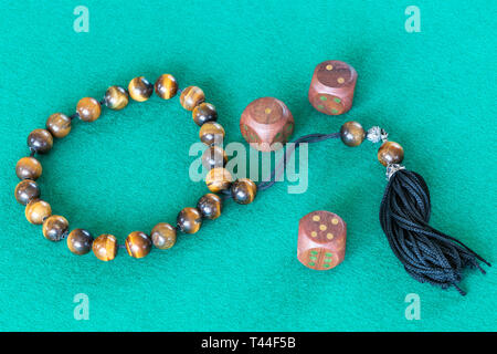 worry beads and three wooden dices with various points on green baize table Stock Photo