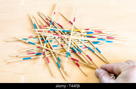 player picks up a stick from pile in Mikado game on wooden board Stock Photo