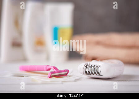 Epilator, shaving razor and wax strips on background with shampoo and towel, selective focus Stock Photo