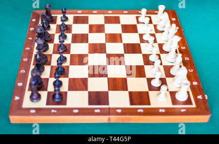 wooden chessboard with chess pieces in starting position on green baize table. Focus on the middle of the board Stock Photo
