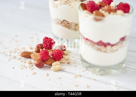Two glasses of greek yogurt granola with raspberries, oatmeal flakes and nuts on white background. Healthy nutrition Stock Photo