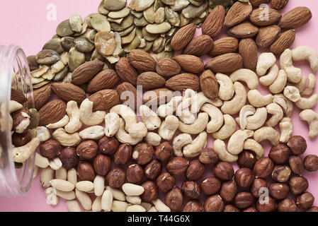 Different types of nuts and seeds in glass jar on pink background, top view Stock Photo