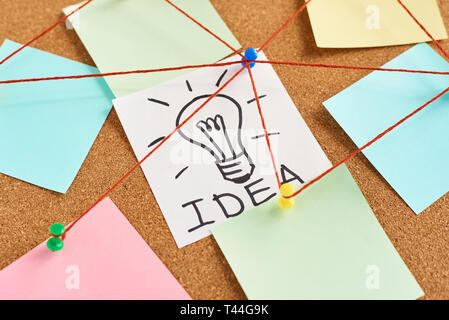 painted light bulb with word idea and colored blank notes on cork board Stock Photo