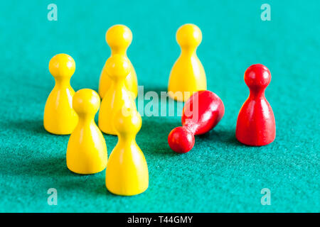concept scene - one standing and one fallen red pawn in front of several yellow pawns on green baize table Stock Photo
