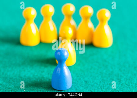 concept scene - one blue pawn in front of several yellow pawns with leader on green baize table. Focus on the blue pawn Stock Photo