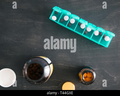 Top view of seven day pill box with pills. Green pill-box with pills visible. Open pill box and jars on dark wooden table. Copy space. Top view or flat lay.Healthy lifestyle and medical concept Stock Photo