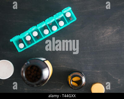 Top view of seven day pill box with pills. Green pill-box with pills visible. Open pill box and jars on dark wooden table. Copy space. Top view or flat lay.Healthy lifestyle and medical concept Stock Photo