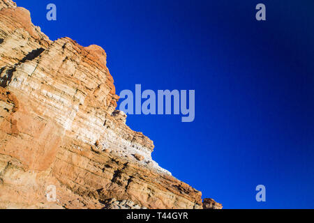 Red and orange rocks form a cliff face above the hot sands of the desert floor. Stock Photo