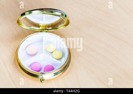 open pillbox with pink and yellow pills on wooden board Stock Photo