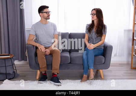 Young Couple Sitting On Sofa Looking At Each Other Stock Photo