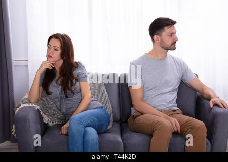 Upset Young Couple Sitting On Sofa At Home Stock Photo