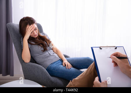 Male Psychologist With Clipboard Sitting Near Young Woman Suffering From Depression Stock Photo