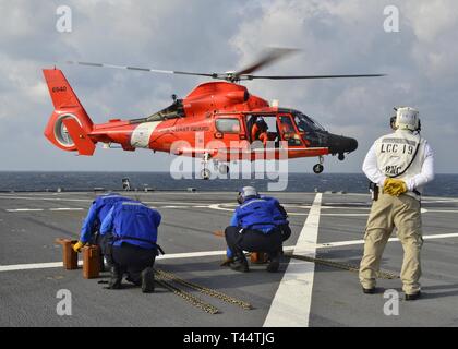 EAST CHINA SEA (Feb. 23, 2019) - U.S. 7th Fleet Flagship USS Blue Ridge (LCC 19) Sailors receive a U.S. Coast Guard helicopter during a joint passenger swap training operation between the Coast Guard and Blue Ridge. Blue Ridge is the oldest operational ship in the Navy and, as 7th Fleet command ship, actively works to foster relationships with allies and partners in the Indo-Pacific Region. Stock Photo