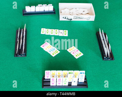 MOSCOW, RUSSIA - APRIL 3, 2019: gameplay of Rummy tile-based card game on green baize table. Rummy is tile and card game based on matching cards of th Stock Photo