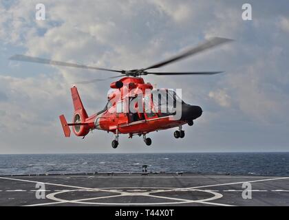 EAST CHINA SEA (Feb. 23, 2019) - A U.S. Coast Guard helicopter lands on the flight deck of U.S. 7th Fleet flagship USS Blue Ridge (LCC 19) during a joint passenger swap training operation between the Coast Guard and Blue Ridge. Blue Ridge is the oldest operational ship in the Navy and, as 7th Fleet command ship, actively works to foster relationships with allies and partners in the Indo-Pacific Region. Stock Photo