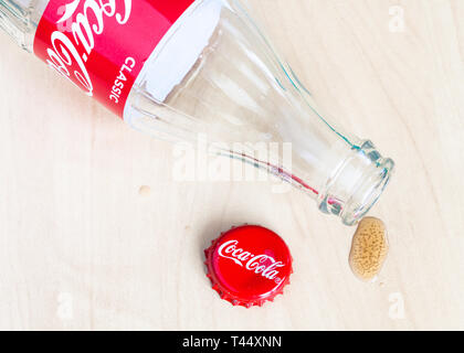 MOSCOW, RUSSIA - APRIL 4, 2019: red crown cap, empty bottle from Coca-Cola beverage and drop of drink on wooden table. Coca-Cola (Coke) is carbonated  Stock Photo