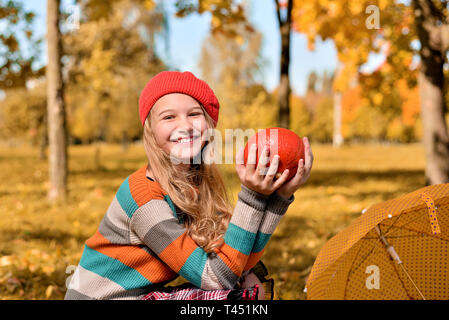 Autumn portrait of happy girl in red hat and sweater. teenager holds an orange pumpkin and smiles Stock Photo