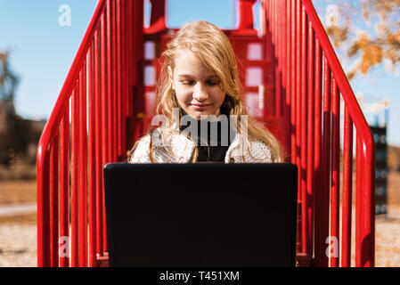 young girl schoolgirl doing lessons. teenager sits on the red stairs in the street Stock Photo