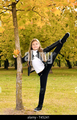 Autumn portrait of little gymnast girl. child shows stretching in the park in nature Stock Photo