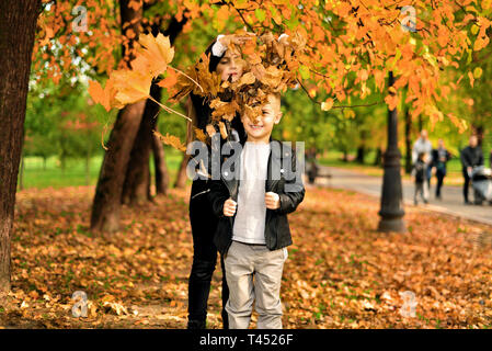 happy brother and sister. funny kids are played. girl throws leaves. little boy smiles contentedly Stock Photo