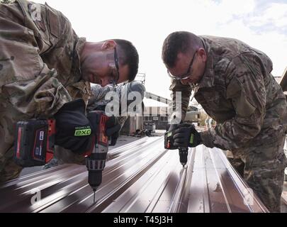MSgt. David Foret and Senior Master Sgt. Kevin Bright, both assigned to the 189th Civil Engineering Squadron, drill holes into metal roofing to prepare it for installation at LIttle Rock Air Force Base, Ark. on February 26, 2019. The 189th and 19th CES are working together to revitalize the base's deployment readiness training grounds. Stock Photo