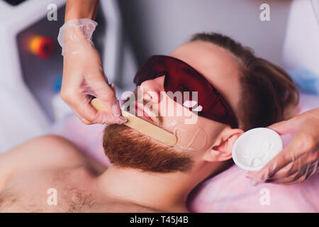 Master doctor performs procedure of removing permanently unwanted facial hair in bearded man with laser. Beauty and health.