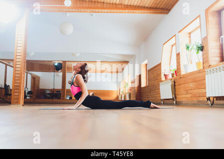 Young yogi attractive woman practicing yoga concept, stretching in Cobra exercise, Bhujangasana pose, working out, wearing sportswear, black tank top Stock Photo
