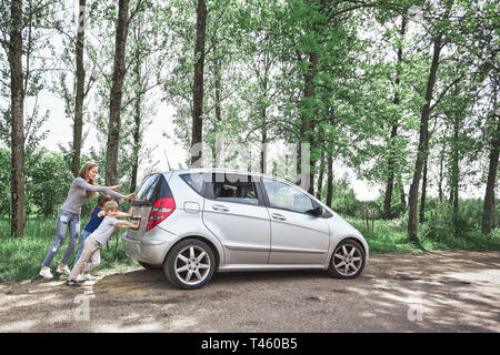 mom, son and daughter pushing a faulty car. adventures on the road Stock Photo