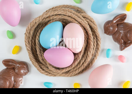 Pink, blue, and purple Easter eggs in nest with chocolate rabbits and jellybeans Stock Photo