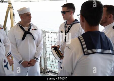 SUNDA STRAIT (March 1, 2019) Engineman Fireman Zachary Kirker, from Mt. Orab, Ohio, assigned to the Avenger-class mine countermeasures ship USS Chief (MCM 14), speaks with Australian sailors before a memorial service aboard the Indonesian Navy (TNI-AL) ship Kri Usman Harun (359). The ceremony was held to honor the American and Australian crews of USS Houston (CA 30) and HMAS Perth (D 29) that lost their lives in battle against the Japanese Imperial Navy during World War II. Stock Photo