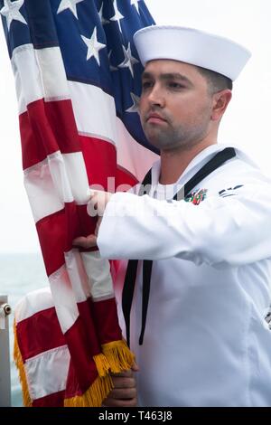 SUNDA STRAIT (March 1, 2019) Hospital Corpsman 2nd Class Edward Navarro, from Riverside, California, holds the Ensign during a memorial service aboard the Indonesian Navy (TNI-AL) ship Kri Usman Harun (359). The ceremony was held to honor the American and Australian crews of USS Houston (CA 30) and HMAS Perth (D 29) that lost their lives in battle against the Japanese Imperial Navy during World War II. Stock Photo
