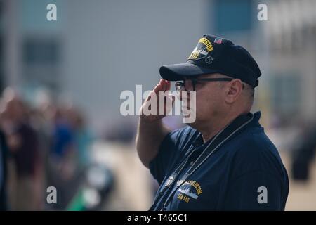 A crewmember from the USS Charleston (LKA-113), an amphibious Navy cargo ship commissioned in 1968, salutes during the new USS Charleston (LCS-18) commissioning ceremony March 2, 2019, in Charleston, S.C. The USS Charleston—a Littoral Combat Ship intended for more shallow waters than typical Navy vessels—is the sixth naval ship named after the city. Although the ship will be stationed in San Diego, CA, the captain and members of the crew will make annual trips to Charleston to interact with the city and work with the Navy League of Charleston to maintain the relationship between the namesake c Stock Photo