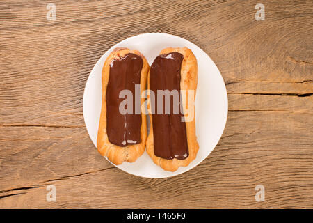 Freshly baked chocolate eclairs on white plate, top view. Stock Photo