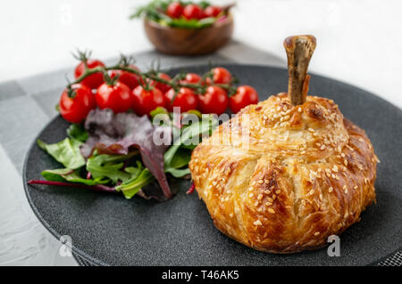 Chicken drumstick in dough baked in the oven with potatoes, tomatoes, onions and spices with a side dish of tomatoes and green salad. Stock Photo