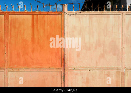 Red colored old rusty entrance metal gate pictured in Taytay, Palawan, Philippines, at daytime. Located behind the gate is an industrial entity. Stock Photo