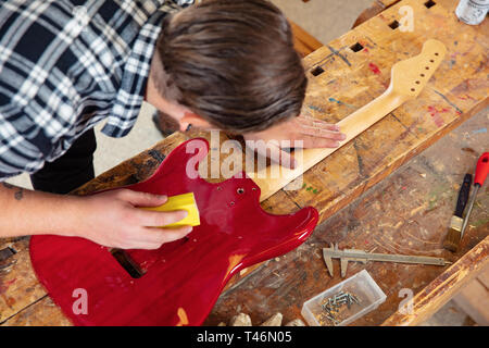 Top view of craftsman sanding a guitar neck in wood at workshop Stock Photo