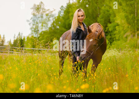 Portrait of woman feeding her arabian horse with snacks in the field Stock Photo
