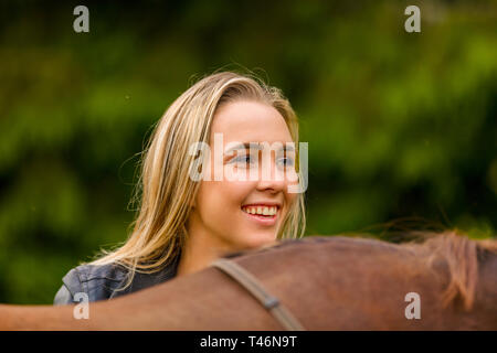 Close-up of smiling woman patting her arabian horse with grass in the field Stock Photo