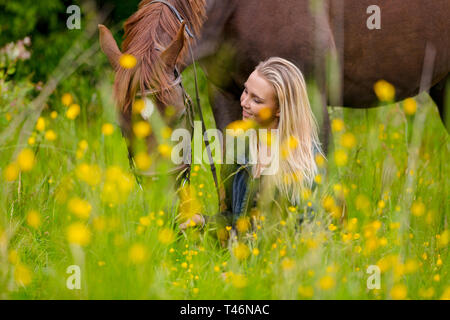 Smiling woman sits in the meadow with her beautiful arabian horse Stock Photo