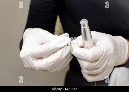 Professional beautician in black with white gloves putting needle on  special tattoo device preparing for permanent make-up in beauty studio, close up Stock Photo
