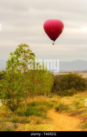 Canberra Australia, March 13th, 2019, hot air balloon flying over colourful fields on a misty morning. Stock Photo