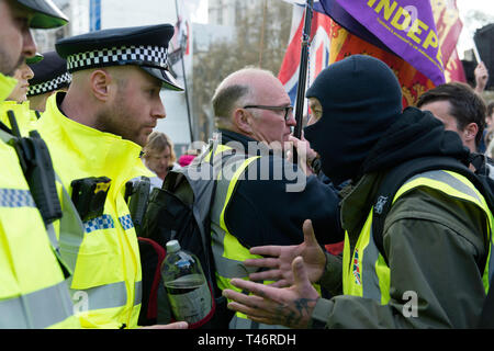 A masked protester seen confronting an officer outside Parliament security fence during the demonstration. Protesters gathered at Parliament Square and marched to different places including Downing Street, Westminster Bridge, Trafalgar Square blocking the streets and confronting the police. Protesters demand from the government and politicians to leave the European Union without a deal and deliver what was promised. Stock Photo