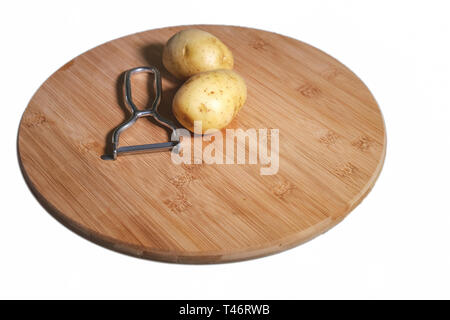 Potatoes on wooden board with a vegetable peeler, close up, isolated on white, copyspace Stock Photo